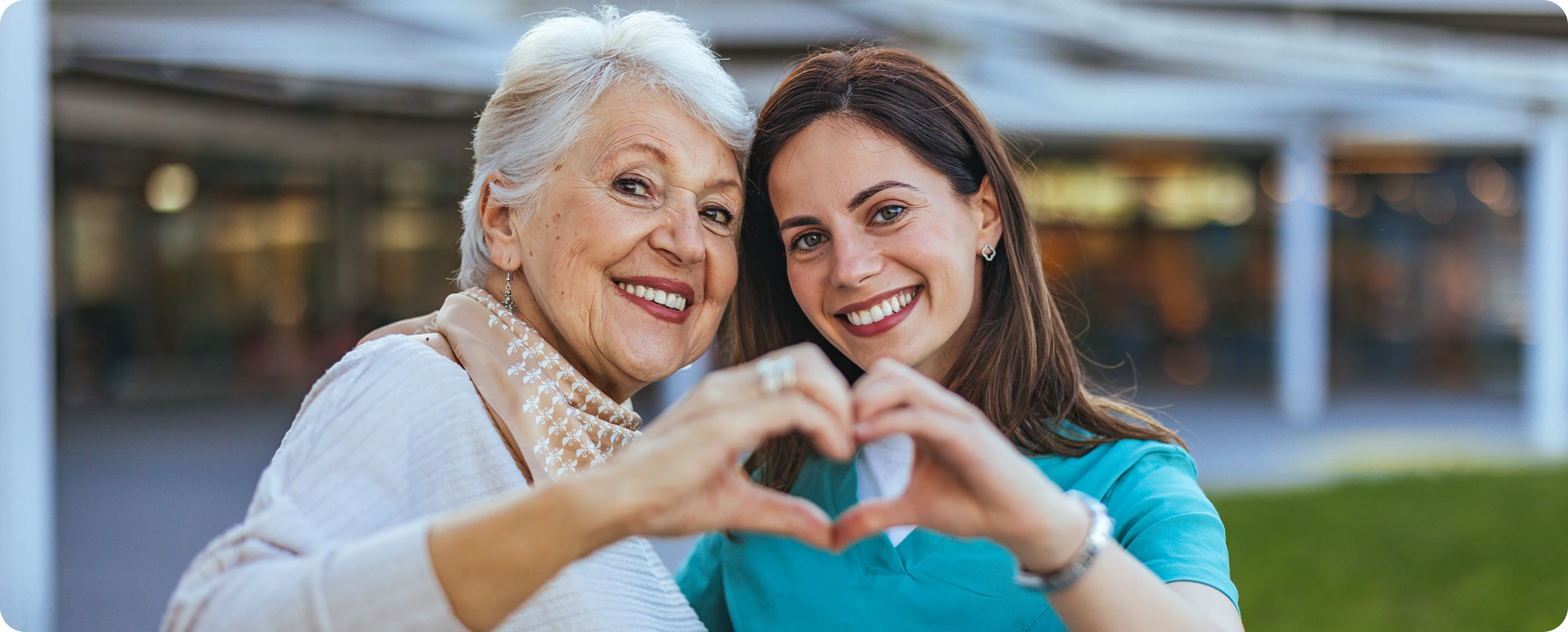 Elderly woman and caregiver forming heart shape.